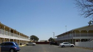 Straßenansicht eines Motels mit mehrstöckigen Gebäuden, einem Parkplatz und blauem Himmel.