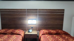 Ein Zimmer mit zwei Betten, einem Holzkopfteil, einem Nachttisch mit Telefon und einem Fenster mit Tageslicht.