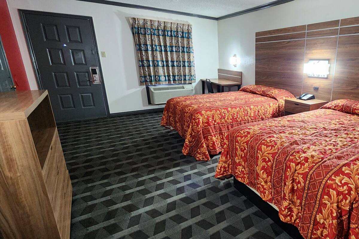 A hotel room with two beds, a desk, a chair, a wardrobe, and a window with curtains.