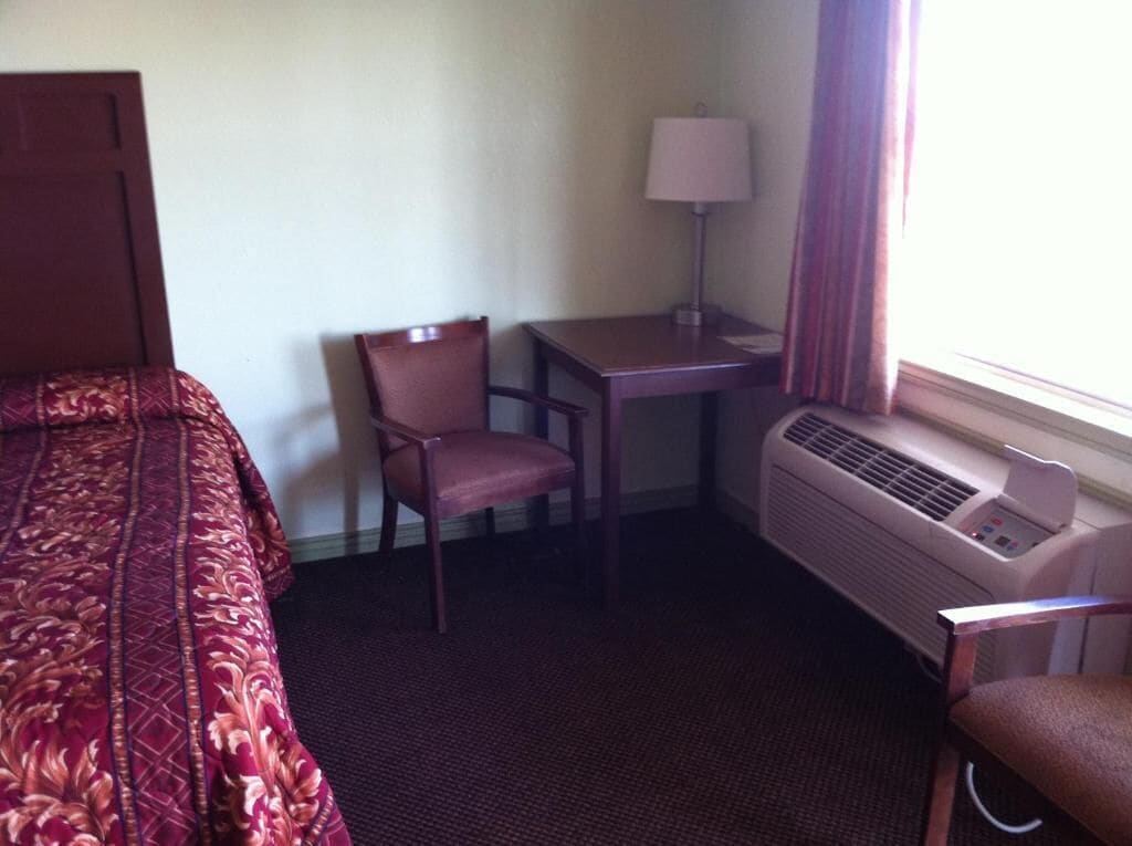 Quarto de hotel com cama, poltrona, escrivaninha, luminária e ar condicionado.