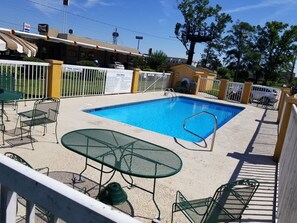 A swimming pool with a fenced area, outdoor seating, and a sign indicating pool capacity. - America's Best Inn (Savannah)