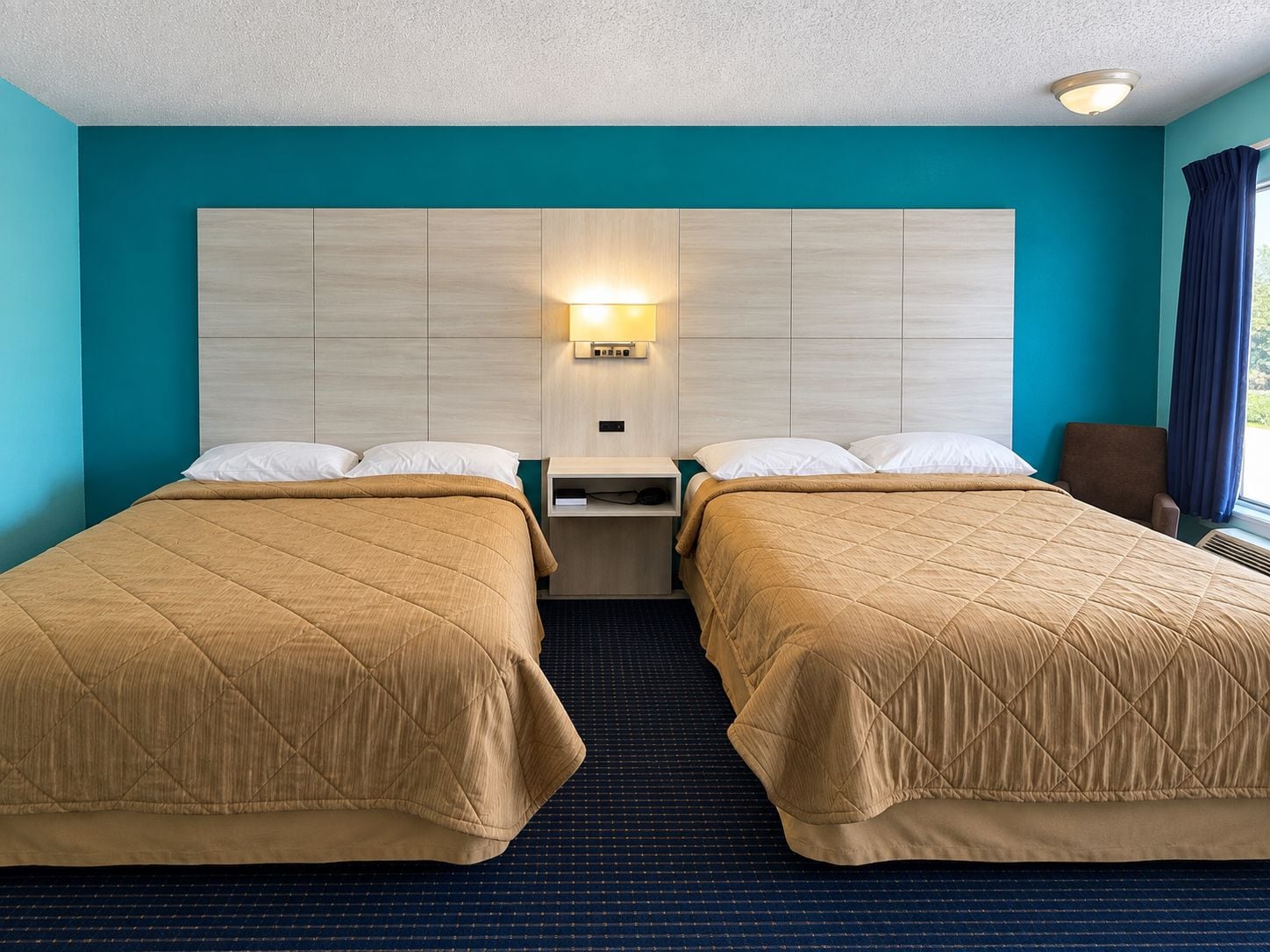 Camera d'albergo con due letti, un comodino, una lampada a parete e una finestra con tende.