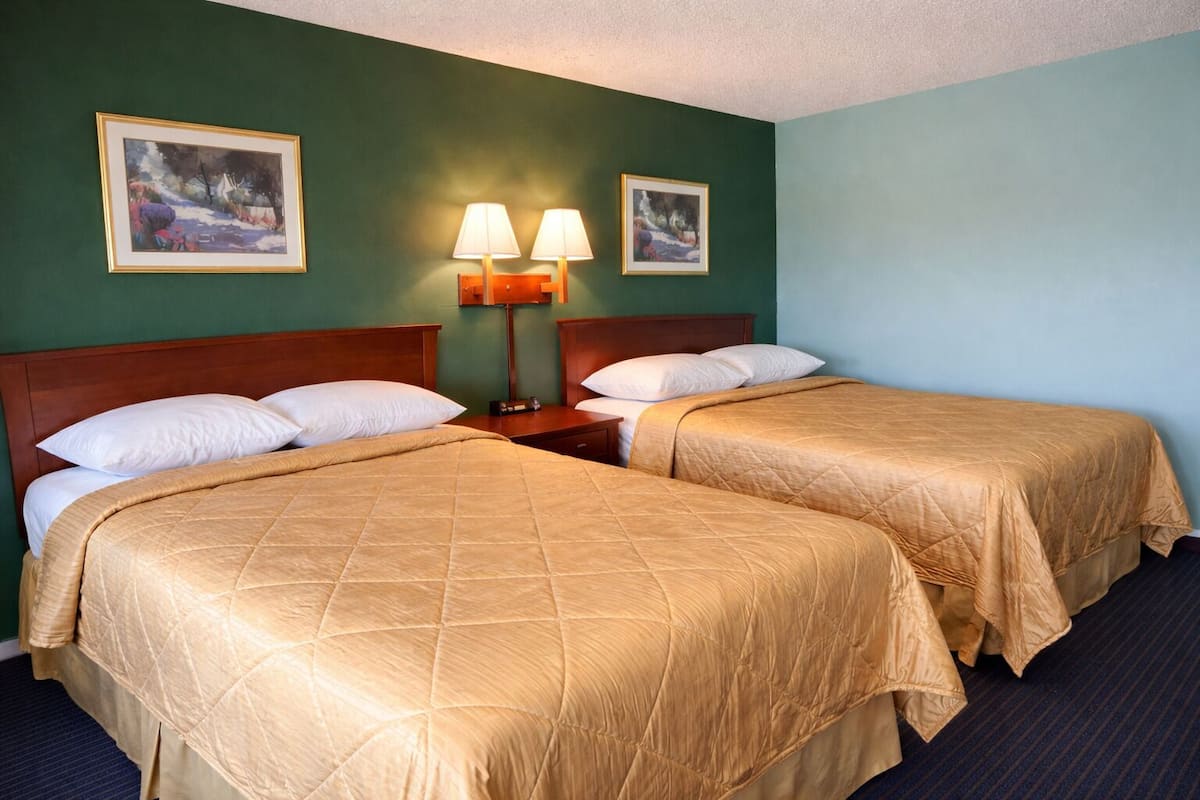 A hotel room with two beds, a nightstand, two wall-mounted lamps, and two framed pictures on the wall.