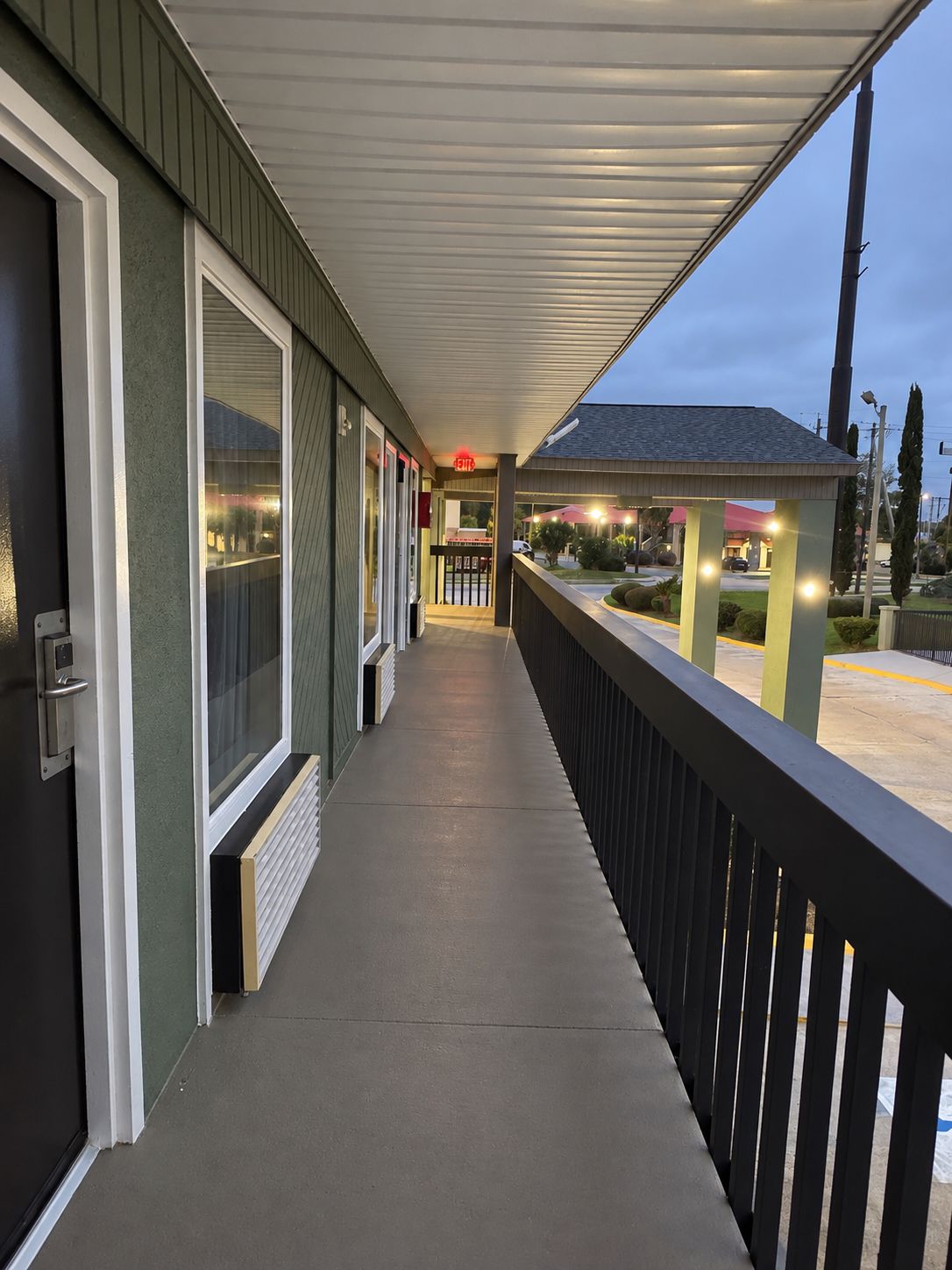 A covered outdoor corridor with a railing, a door, and a small building in the background.