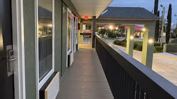 A covered outdoor corridor with a railing, a door, and a small building in the background.