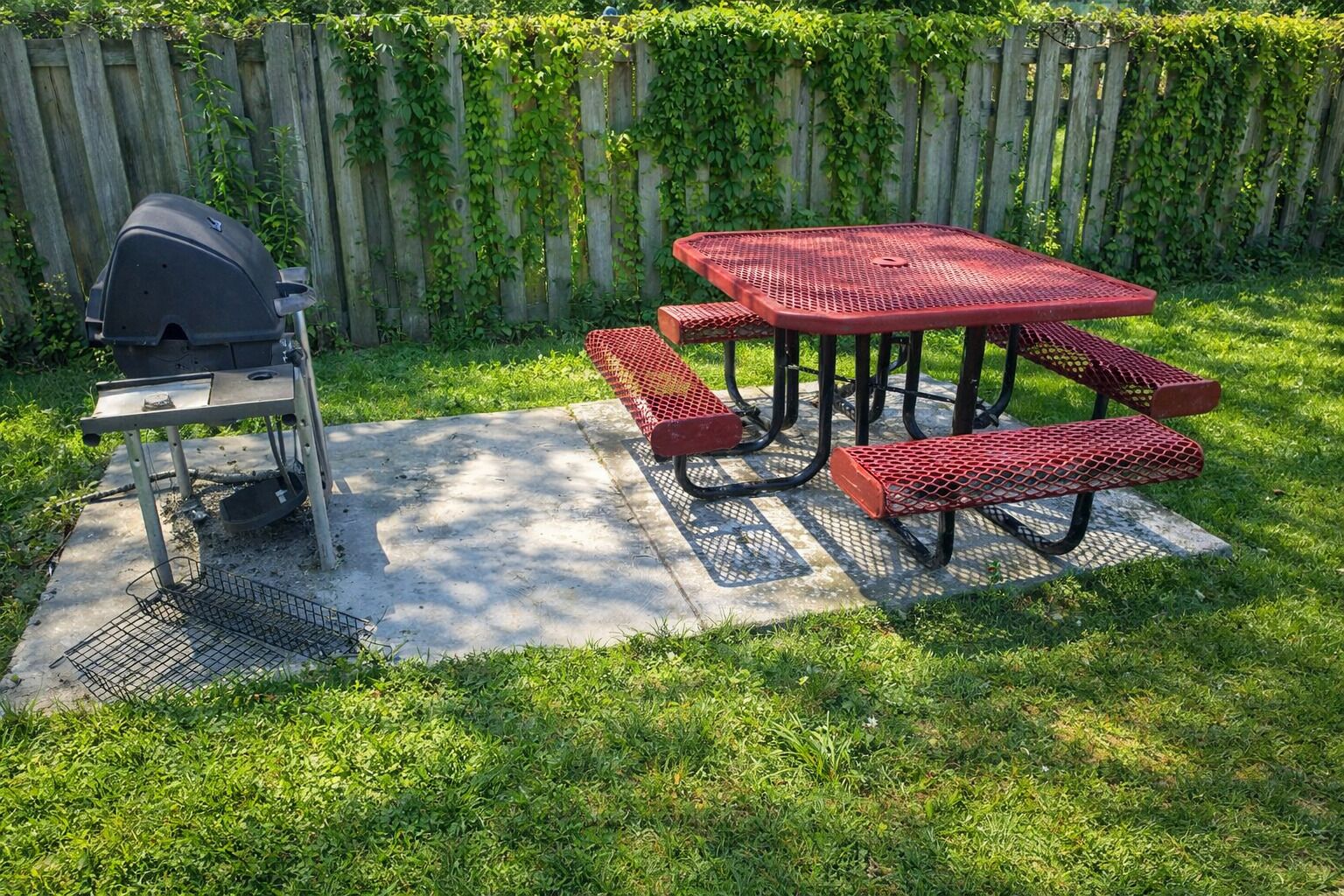 A patio with a grill, a red metal table, and benches.