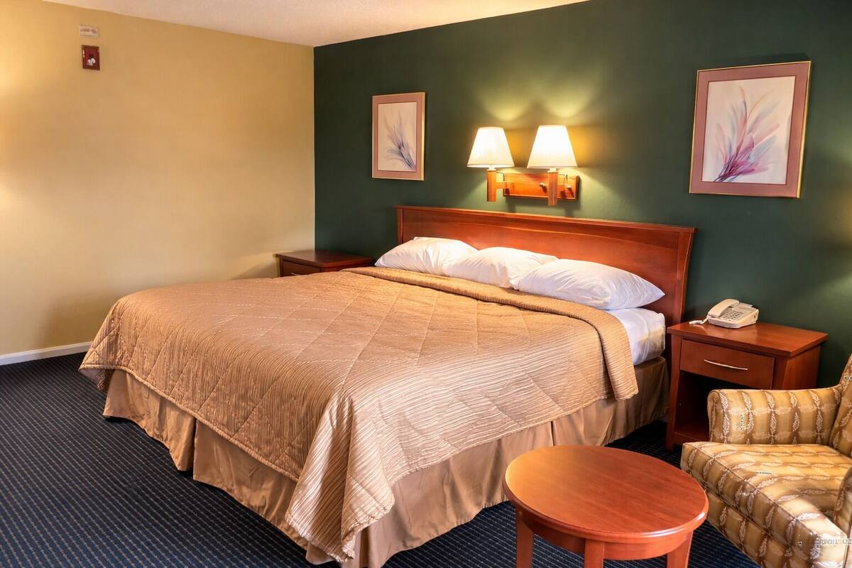 A hotel room with a large bed, bedside lamps, a telephone, a chair, and artwork on the walls.