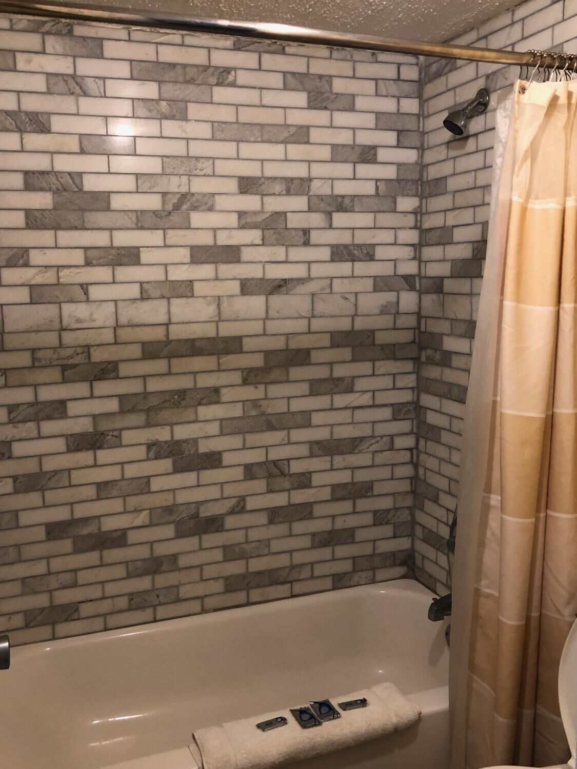 A bathroom with a tiled shower wall, a bathtub, and a beige shower curtain.