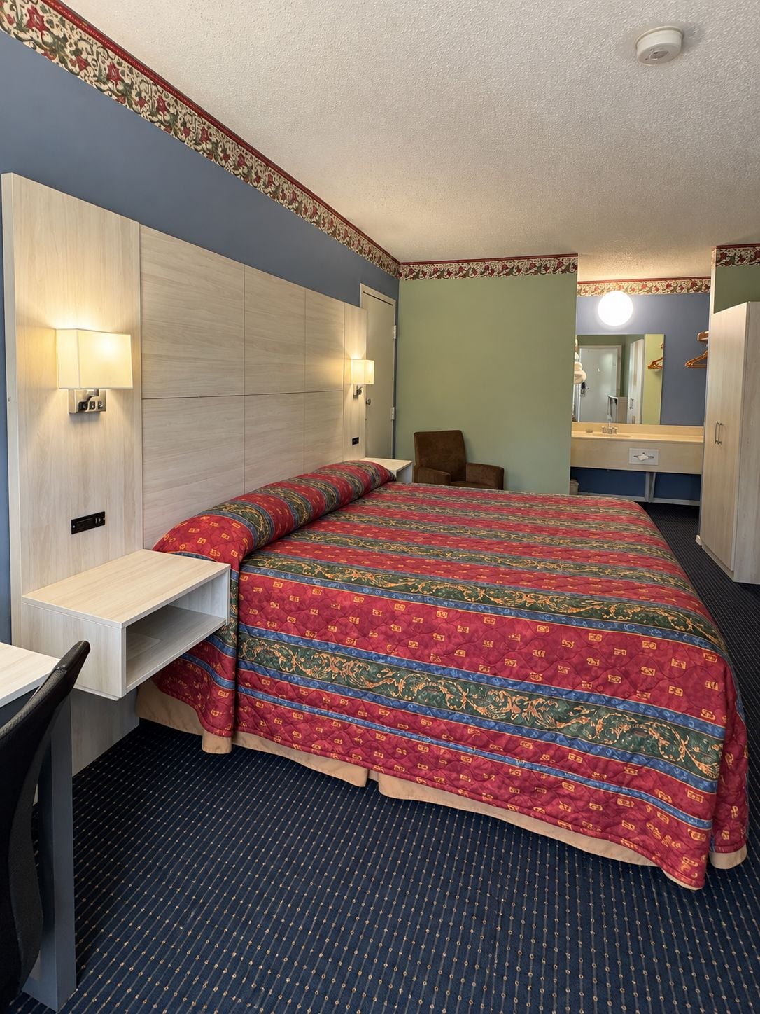 Una camera d'albergo con un letto, una scrivania, una sedia, uno specchio e un armadio.