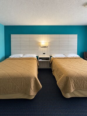 A hotel room with two beds, a nightstand, and a wall-mounted lamp. - America's Best Inn (Savannah)