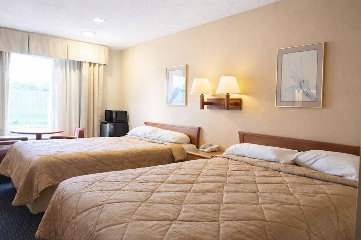 A hotel room with two beds, a desk, a chair, a TV, and two wall-mounted lamps.