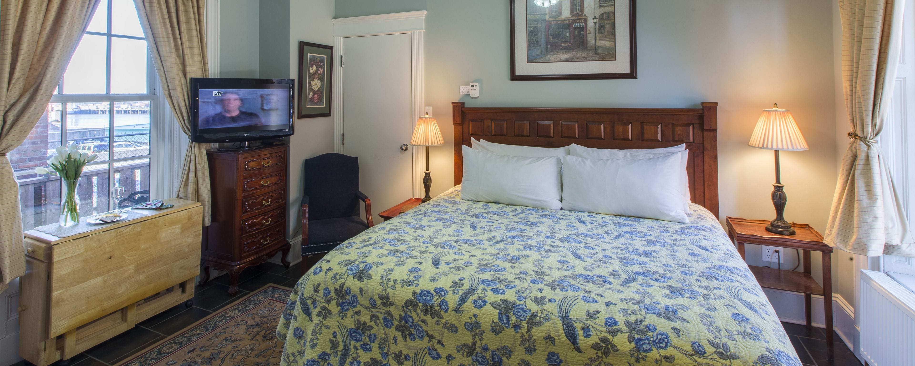 A hotel room with a bed, a TV, a dresser, a chair, and two bedside lamps.