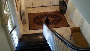 Una imponente escalera con barandilla negra, que conduce a un rellano con un tapete estampado y un sillón marrón.
