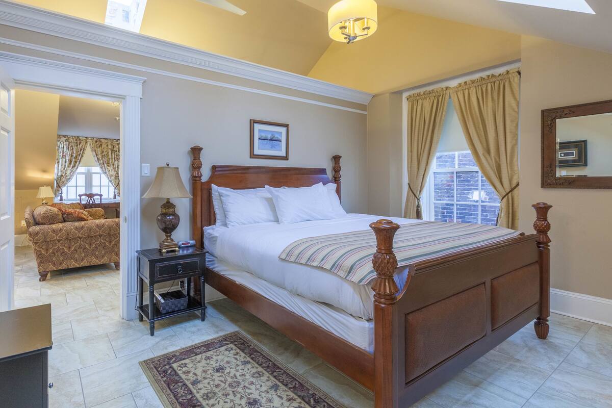 A bedroom with a wooden bed, a nightstand, a lamp, a window with curtains, and a ceiling fan.