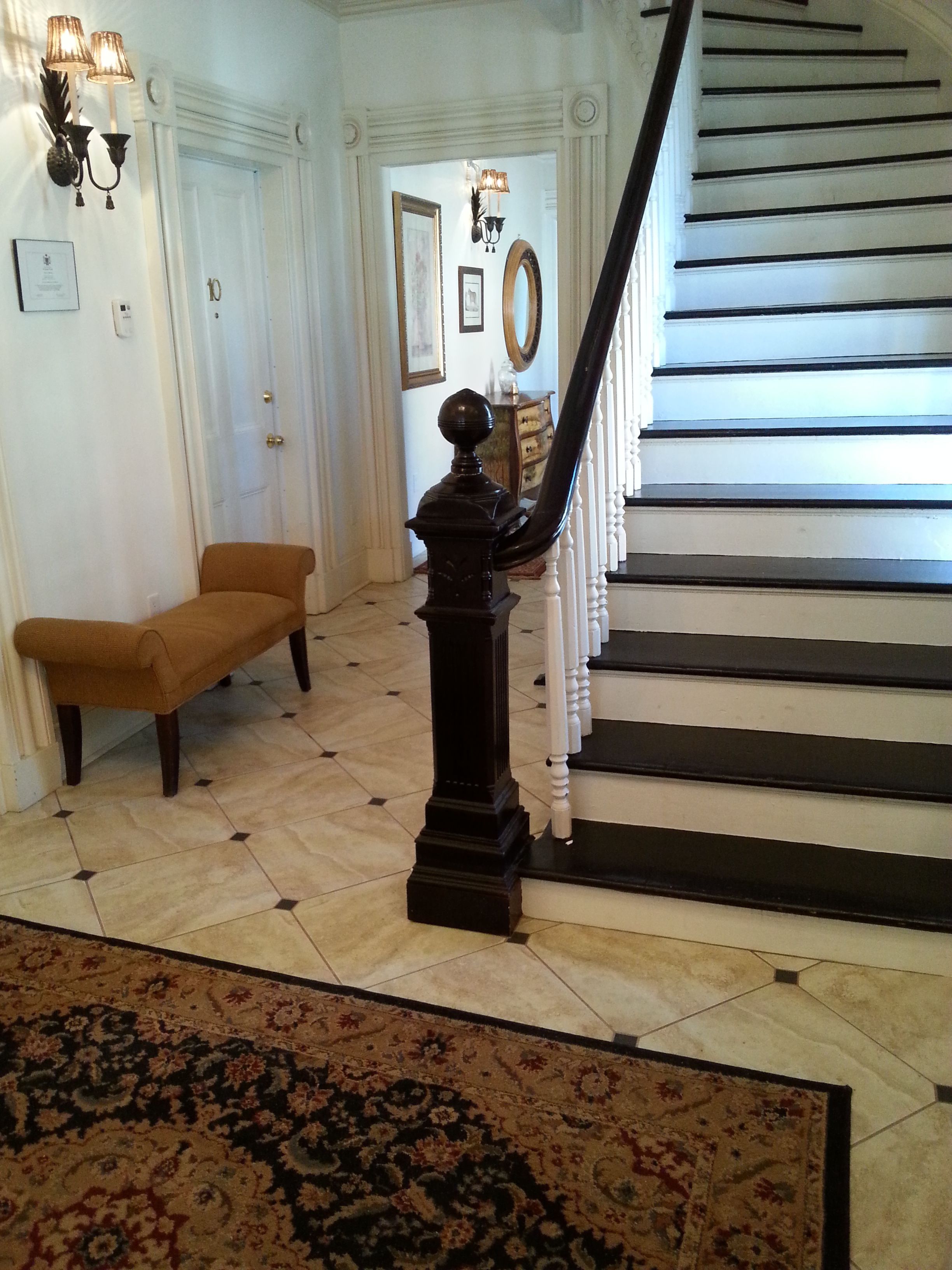 Un grand escalier orné d’une balustrade noire, un banc en bois et un tapis à motifs sur le sol.