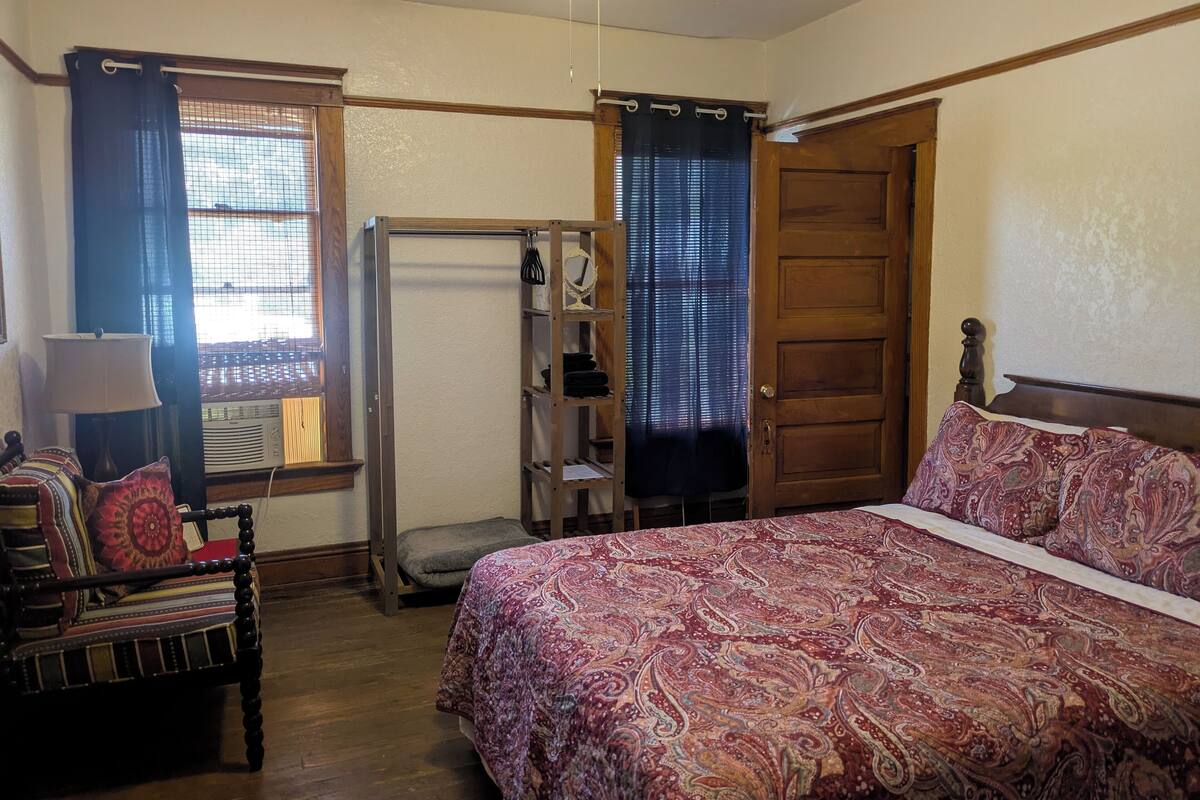 A bedroom with a bed, a chair, a shelf, and a wardrobe.