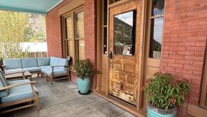 Un patio couvert avec une porte en bois, deux plantes en pot et un canapé bleu.