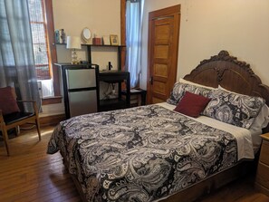 Un dormitorio con cama, escritorio, silla, refrigerador y ventana con cortinas.