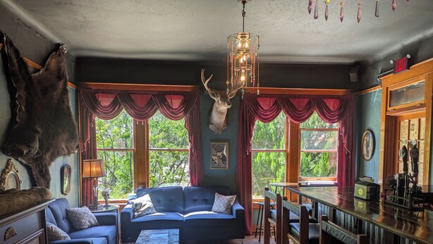 Un intérieur rustique, avec une grande tête de cerf accrochée au mur, un ensemble de canapés bleus, une table à manger en bois et un lustre.