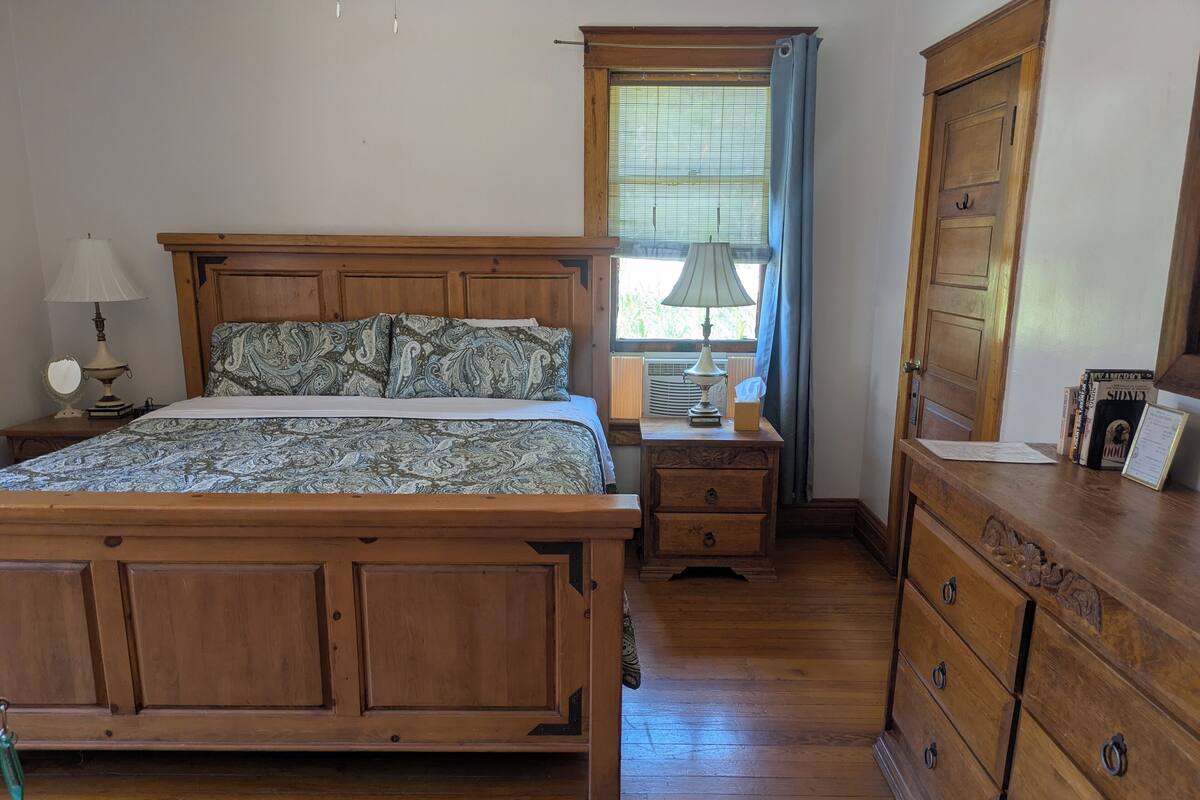 A bedroom with a wooden bed, nightstands, a dresser, and a window with curtains.