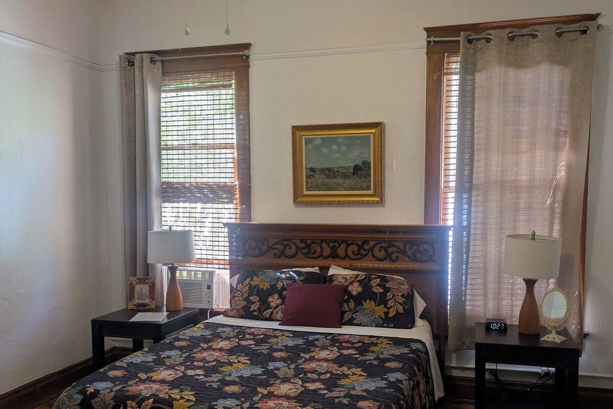 A bedroom with a bed, a nightstand, a bedside table, a ceiling fan, and a window with curtains.