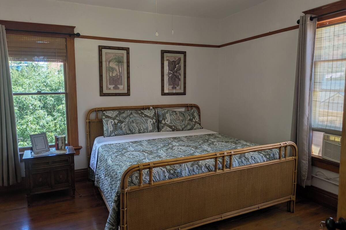 A bedroom with a wooden bed, two framed pictures on the wall, a bedside table with a lamp, and a window with curtains.