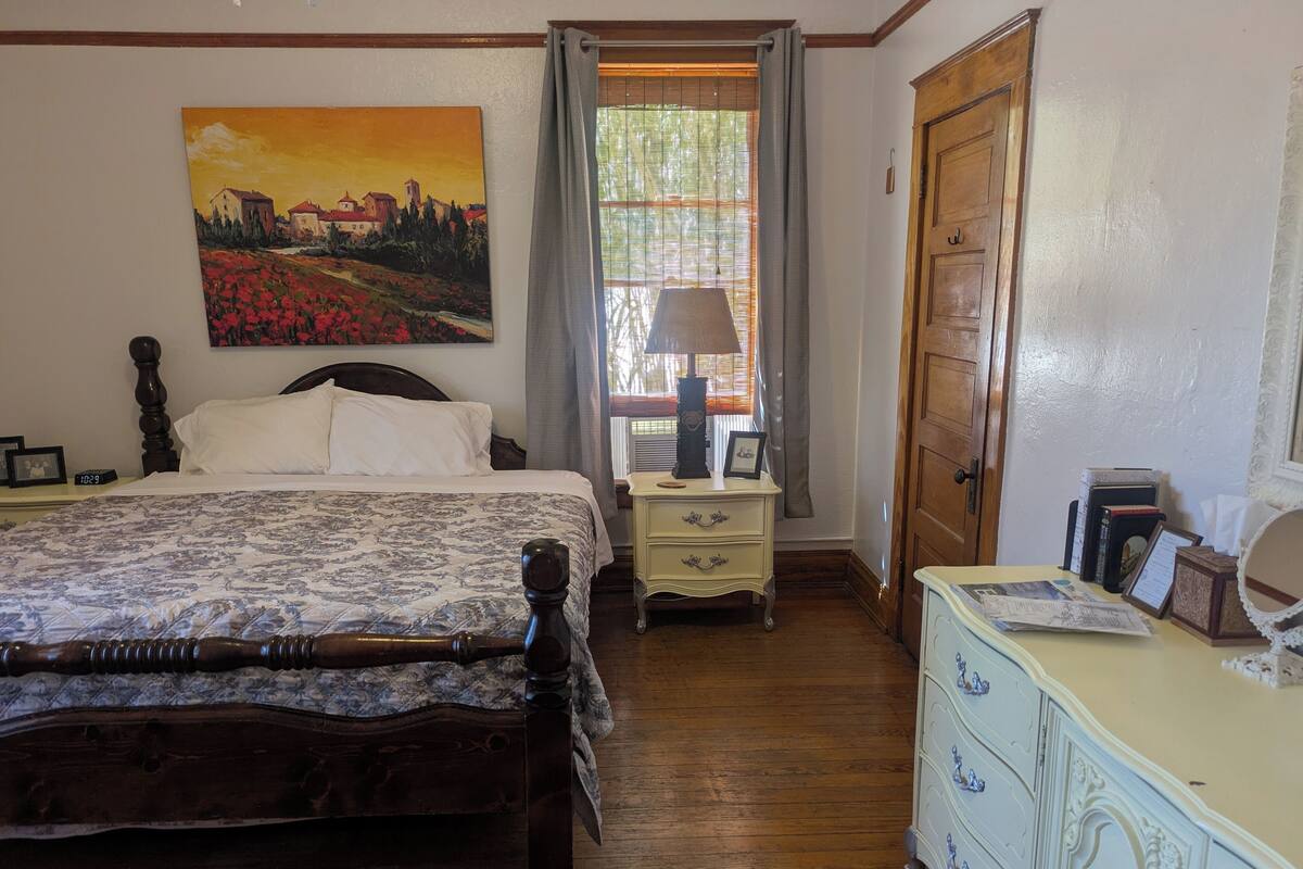 A bedroom with a wooden bed, a nightstand with a lamp, a dresser, and a painting on the wall.