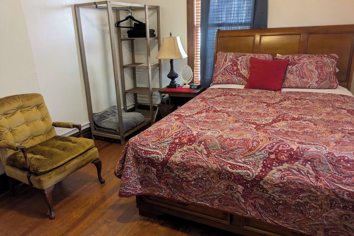 A bedroom with a bed, a chair, a wardrobe, and a nightstand.
