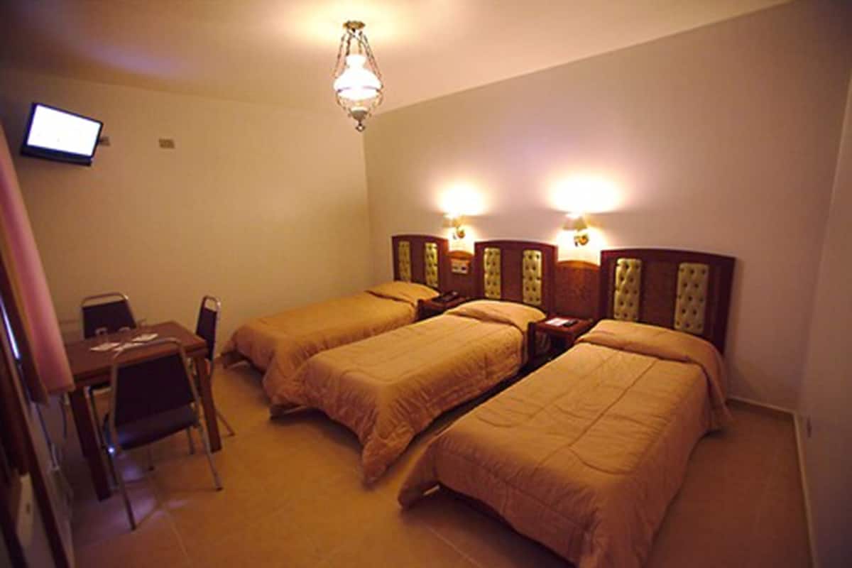 A hotel room with three single beds, a desk with a chair, and a television on the wall.