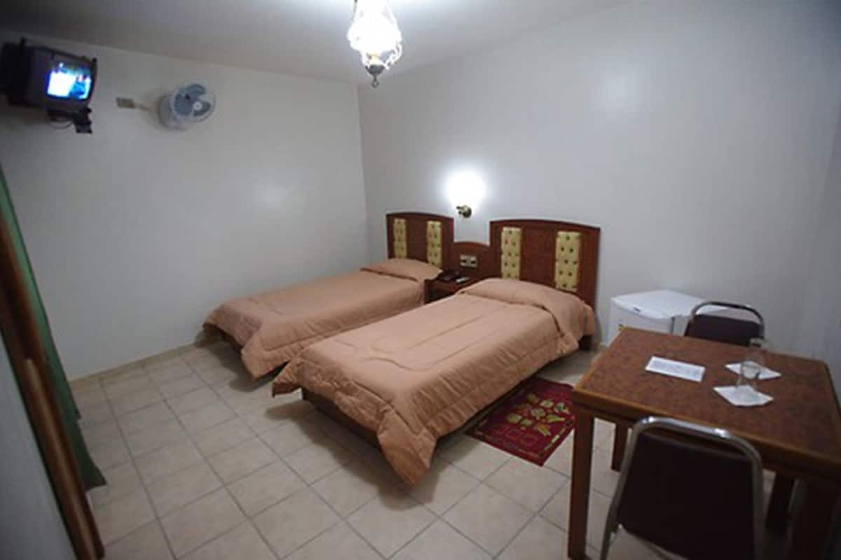 A room with two beds, a desk, a chair, a television, and a ceiling fan.