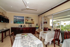 A dining area with tables set for two, a ceiling fan, and a view through a glass door. - Chartwell Guest House (Umhlanga)