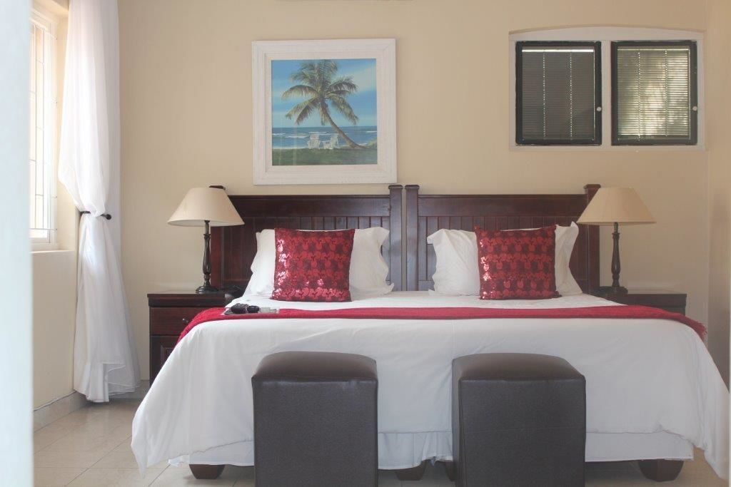 A hotel room with a bed, two bedside tables, a nightstand, a framed picture on the wall, and a window with blinds.