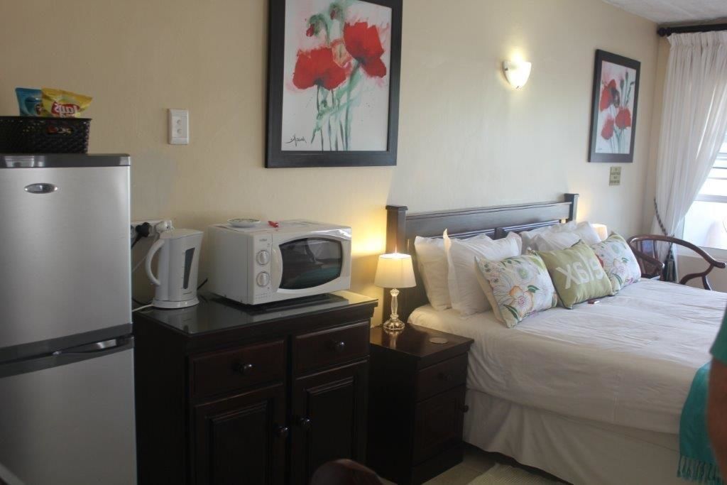 Una habitación de hotel con una cama, una mesita de noche con lámpara, microondas, hervidor de agua y refrigerador.