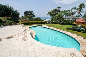 A swimming pool with a curved edge, surrounded by a tiled patio. - Chartwell Guest House (Umhlanga)