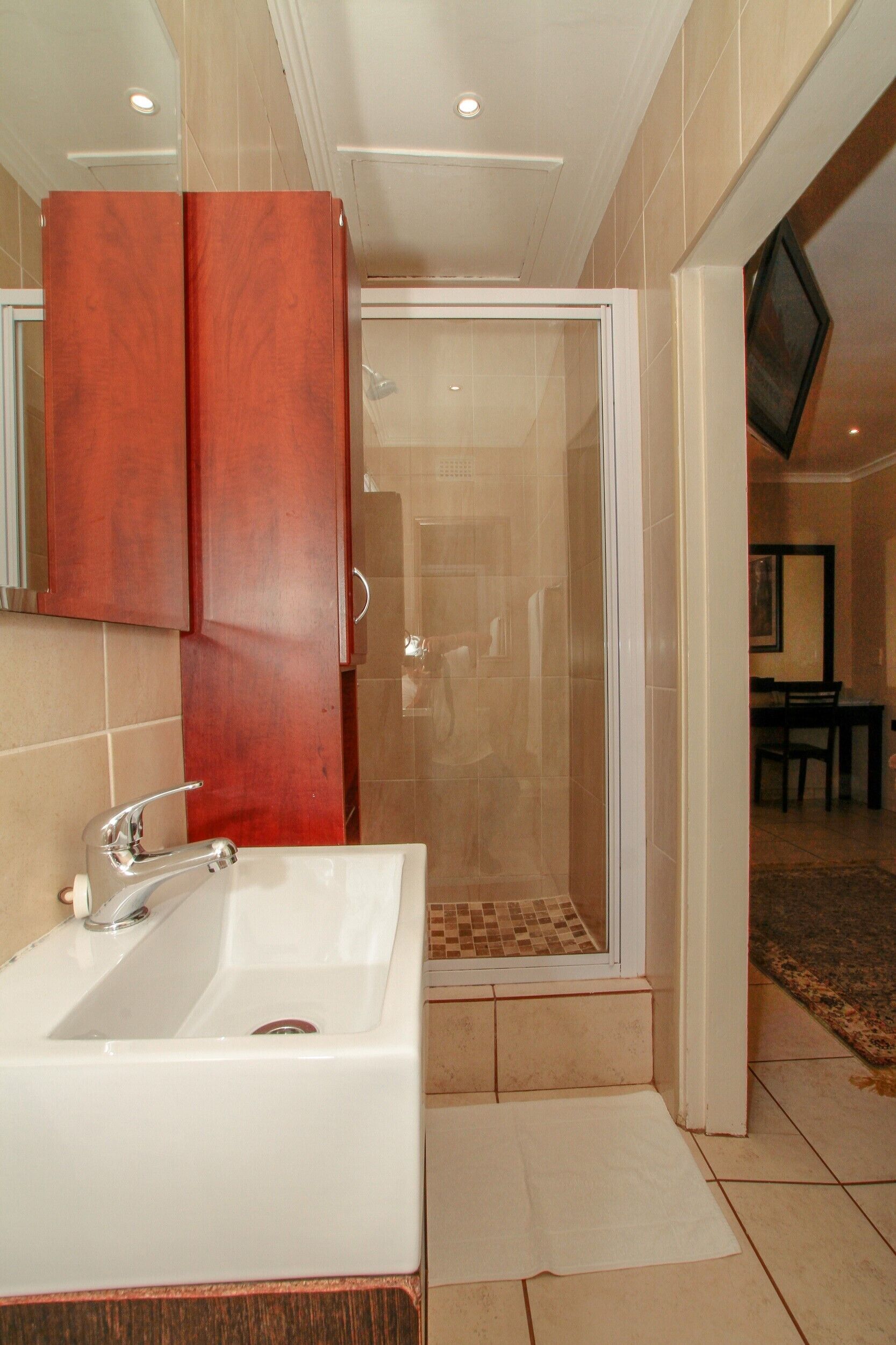 Une salle de bain avec un lavabo blanc, des meubles en bois et une cabine de douche en verre.