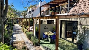 A modern house with a covered patio, a dining area with blue chairs, and a green outdoor floor. - Pelican Lodge (Sedgefield)