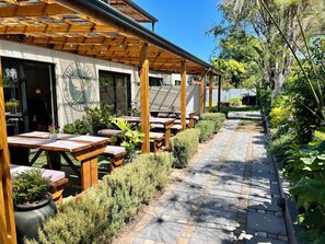 An outdoor patio area with wooden tables and benches, surrounded by potted plants and a stone pathway. - Pelican Lodge (Sedgefield)