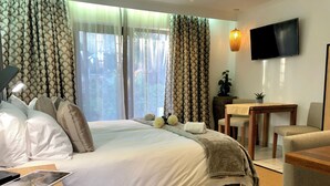 Habitación de hotel con una cama grande, un escritorio, una silla, un televisor y una ventana con cortinas.