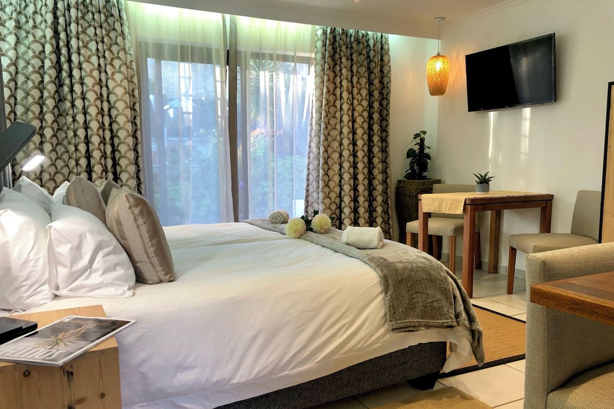 A hotel room with a large bed, a desk, a chair, a television, and a window with curtains.