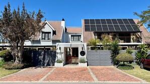 Una casa moderna de dos pisos con techo de paneles solares, entrada de vehículos y jardín bien cuidado.