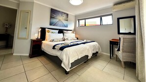 A bedroom with a bed, a nightstand, a lamp, a window, a mirror, and a picture on the wall. - Pelican Lodge (Sedgefield)