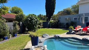 A backyard with a swimming pool, a patio with red chairs, and various potted plants. - Pelican Lodge (Sedgefield)