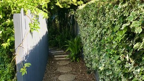 Un estrecho sendero de jardín con piedras para pisar que atraviesa abundante vegetación y una cerca azul a un lado.
