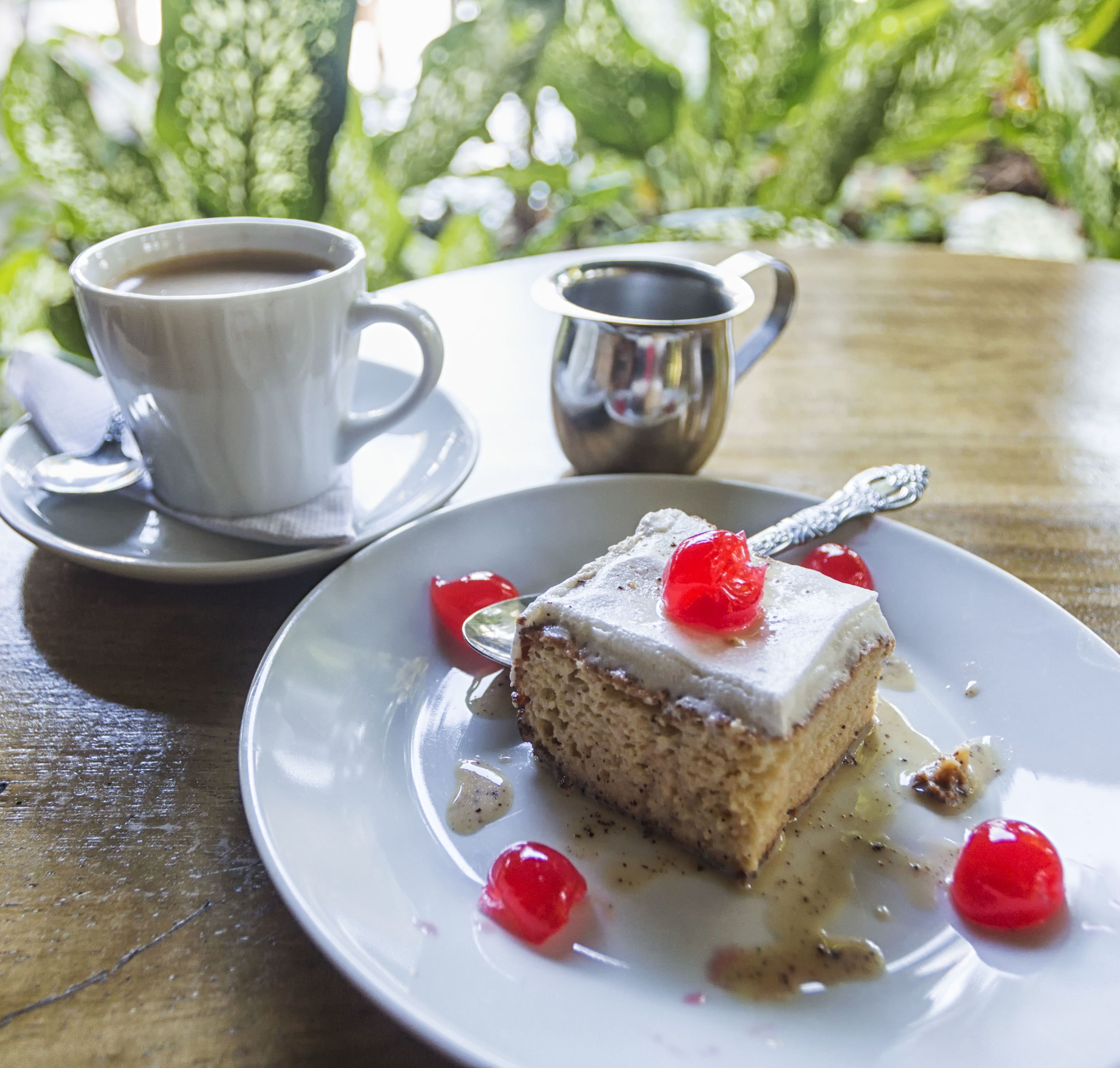 Un plato de postre con una porción de pastel, cerezas y una taza de café sobre una mesa.