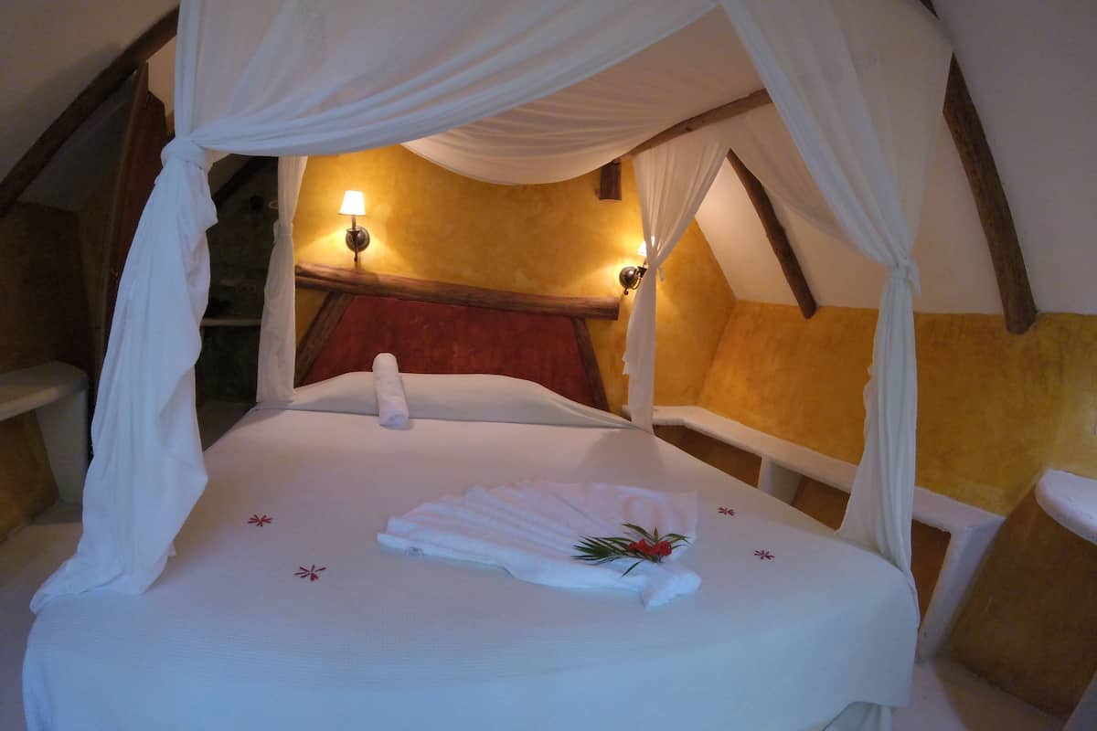 A bed with a canopy, a red chair, and a wall-mounted lamp.