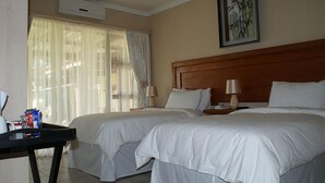 A hotel room with two beds, a wooden headboard, a table with a lamp, and a window with sheer curtains. - Mountain View Guest House (Glencoe)