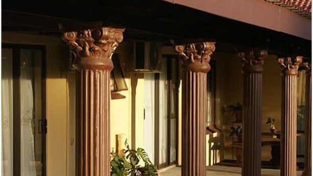 A covered outdoor area with classical columns, potted plants, and a clear view of the building's entrance. - Mountain View Guest House (Glencoe)