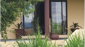 A building with a beige exterior, a glass door, and a column. There are potted plants and tall grasses in front. - Mountain View Guest House (Glencoe)