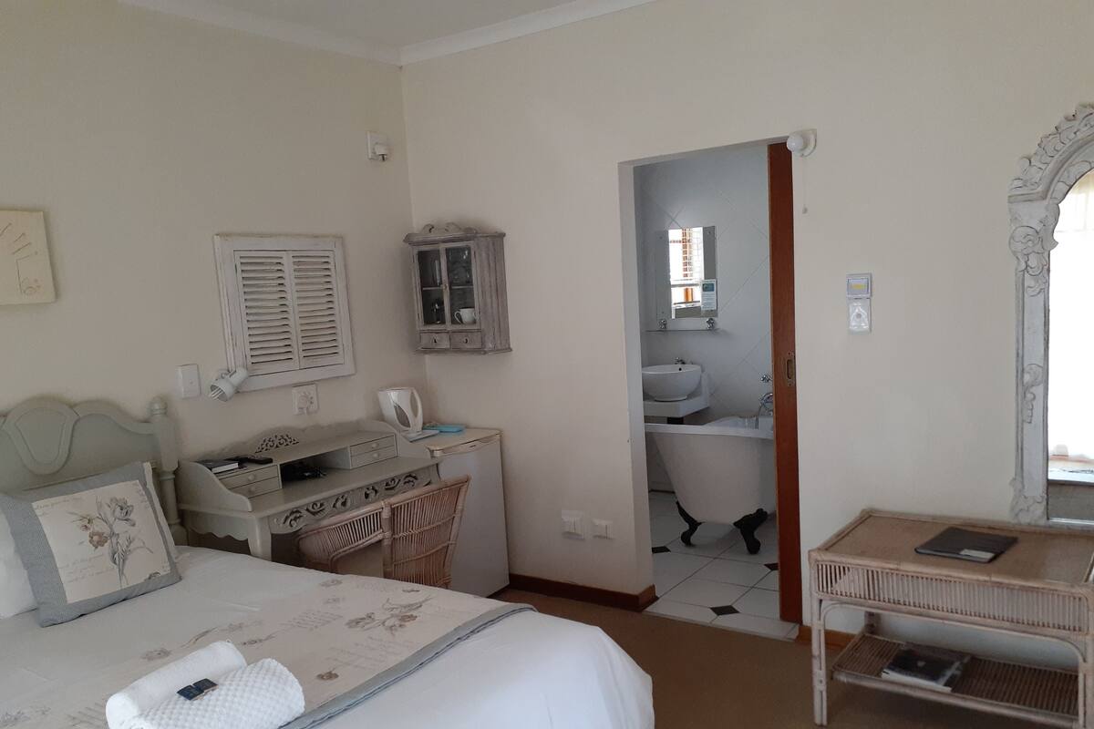 Ein Schlafzimmer mit Bett, Schreibtisch, Stuhl, einem kleinen Tisch und einem durchgegangenen Tür sichtbaren Badezimmer.