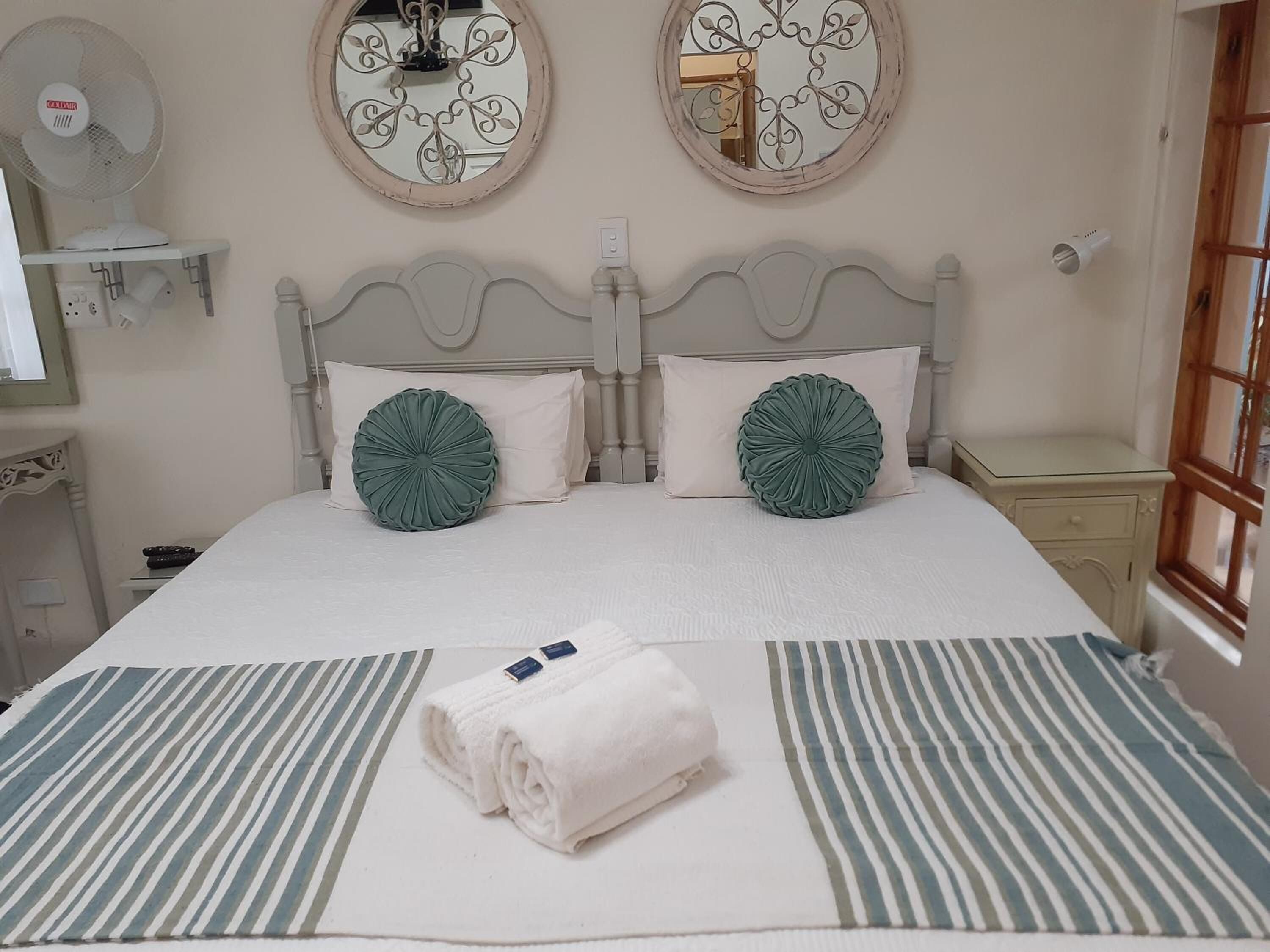 A neatly made bed with two decorative pillows, a striped area rug, and a folded towel on the bed.